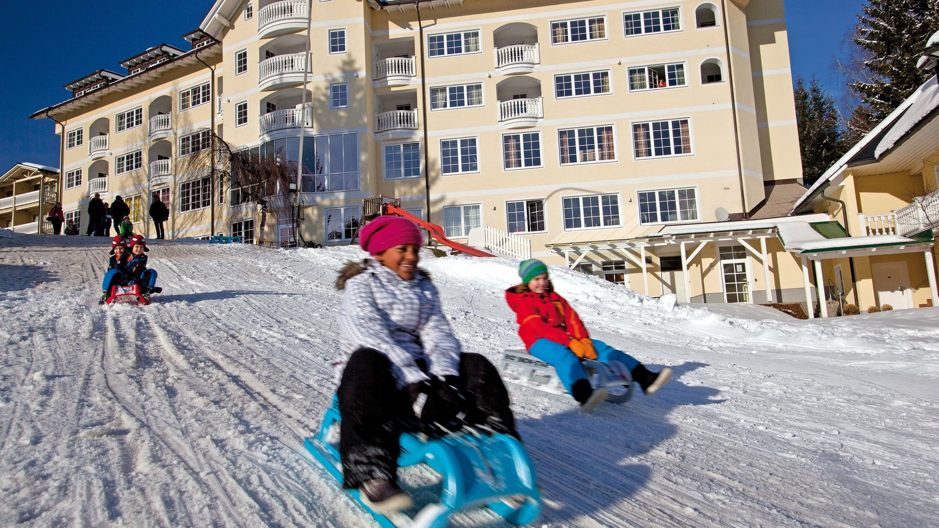 Children tobogganing on a slope in front of the Hotel Dilly