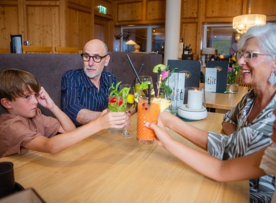 Familie stoßt mit Getränken an der Bar im Hotel Dilly an